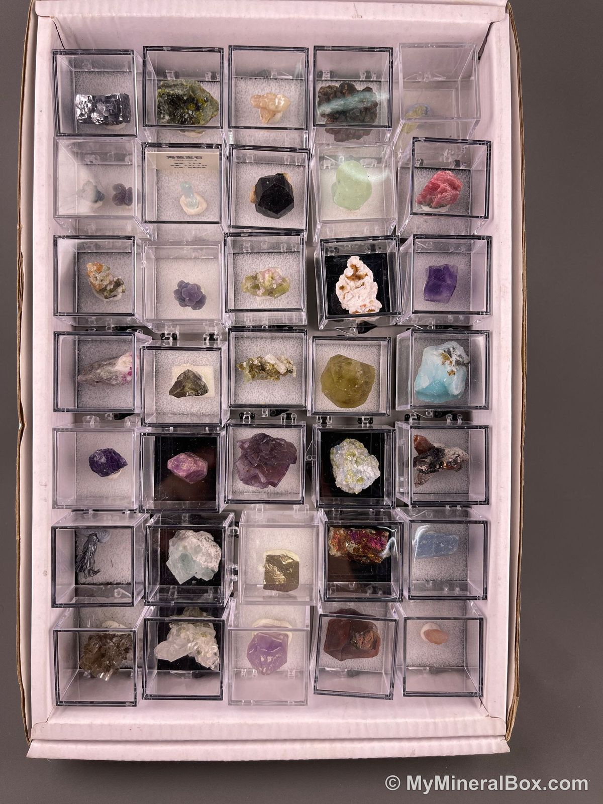 Bulk002 actual mixed mineral specimen box with approximately 35 to 40 different mini specimens in clear display boxes, including likely fluorite, quartz, aquamarine, galena, pyrite, grape agate, stibnite and other assorted minerals.