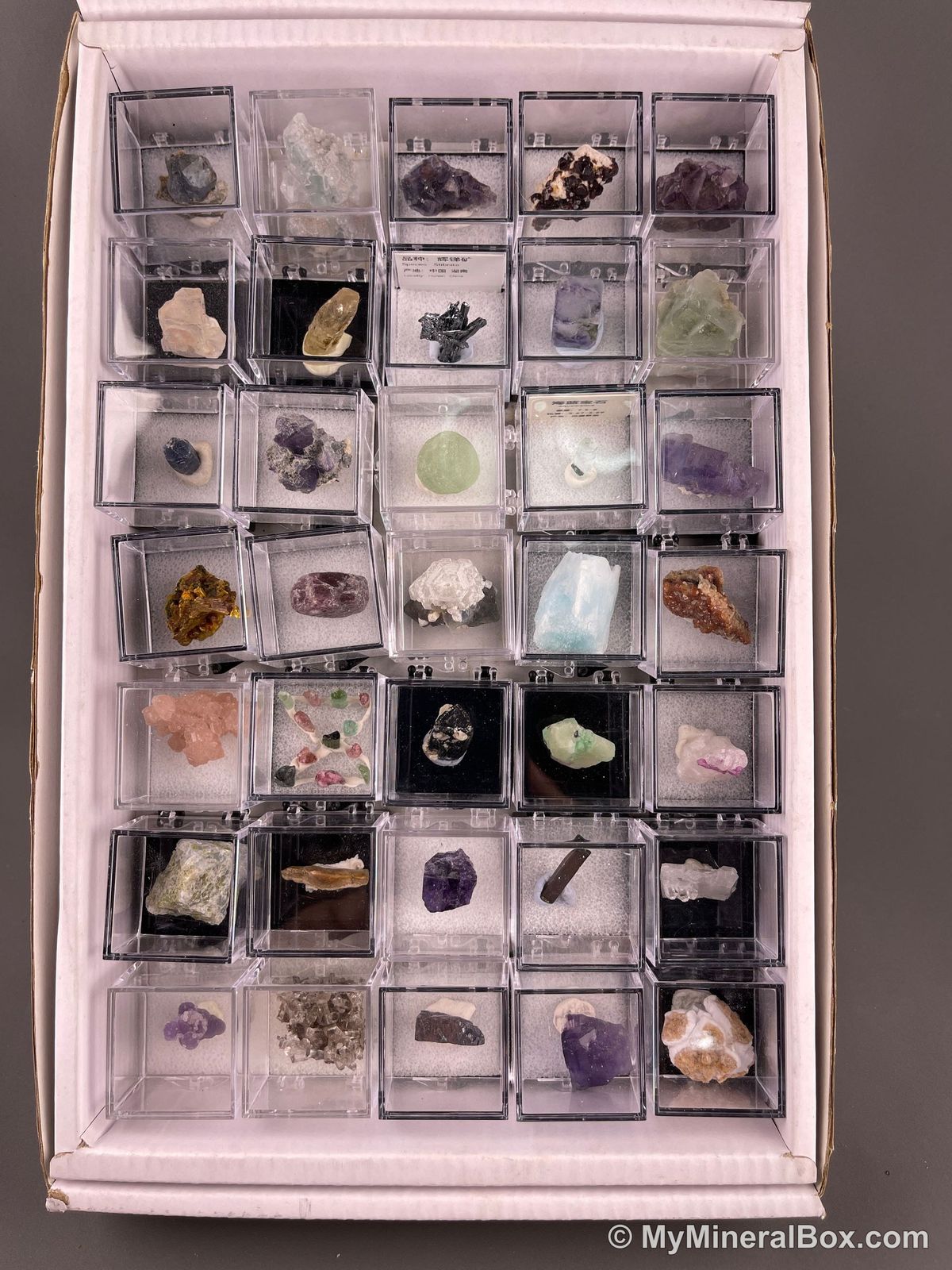 Bulk003 actual mixed mineral specimen box with about 35 different mini natural specimens, including likely fluorite, garnet, stibnite, quartz, aquamarine, tourmaline and grape agate.