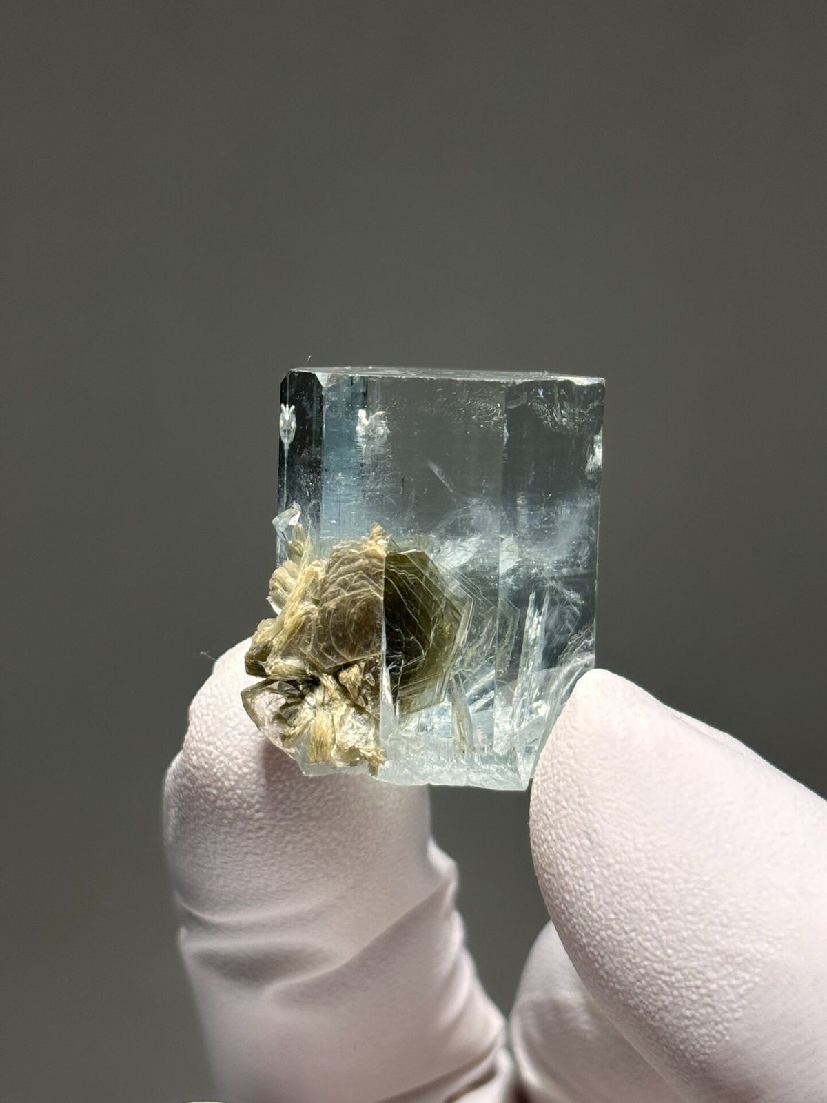 Gem aquamarine with mica grown half inside it from Pakistan, held in gloved hand