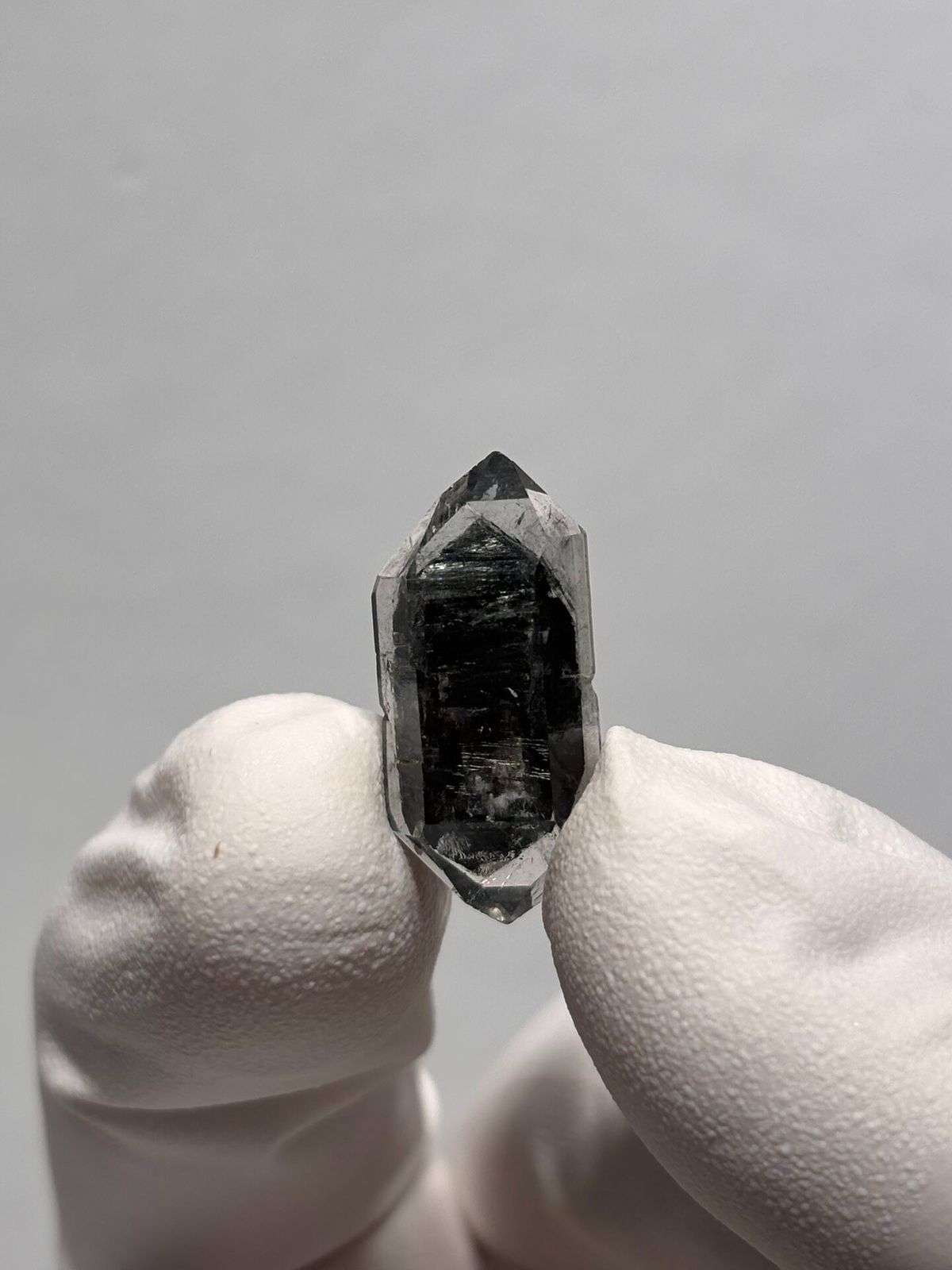 Tiny black sugar-core double-terminated quartz from Yunnan, China, held in gloved hand