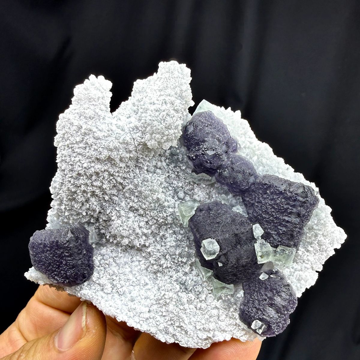 Muted purple recrystallised fluorite balls on white druse from Fujian, China, held in hand