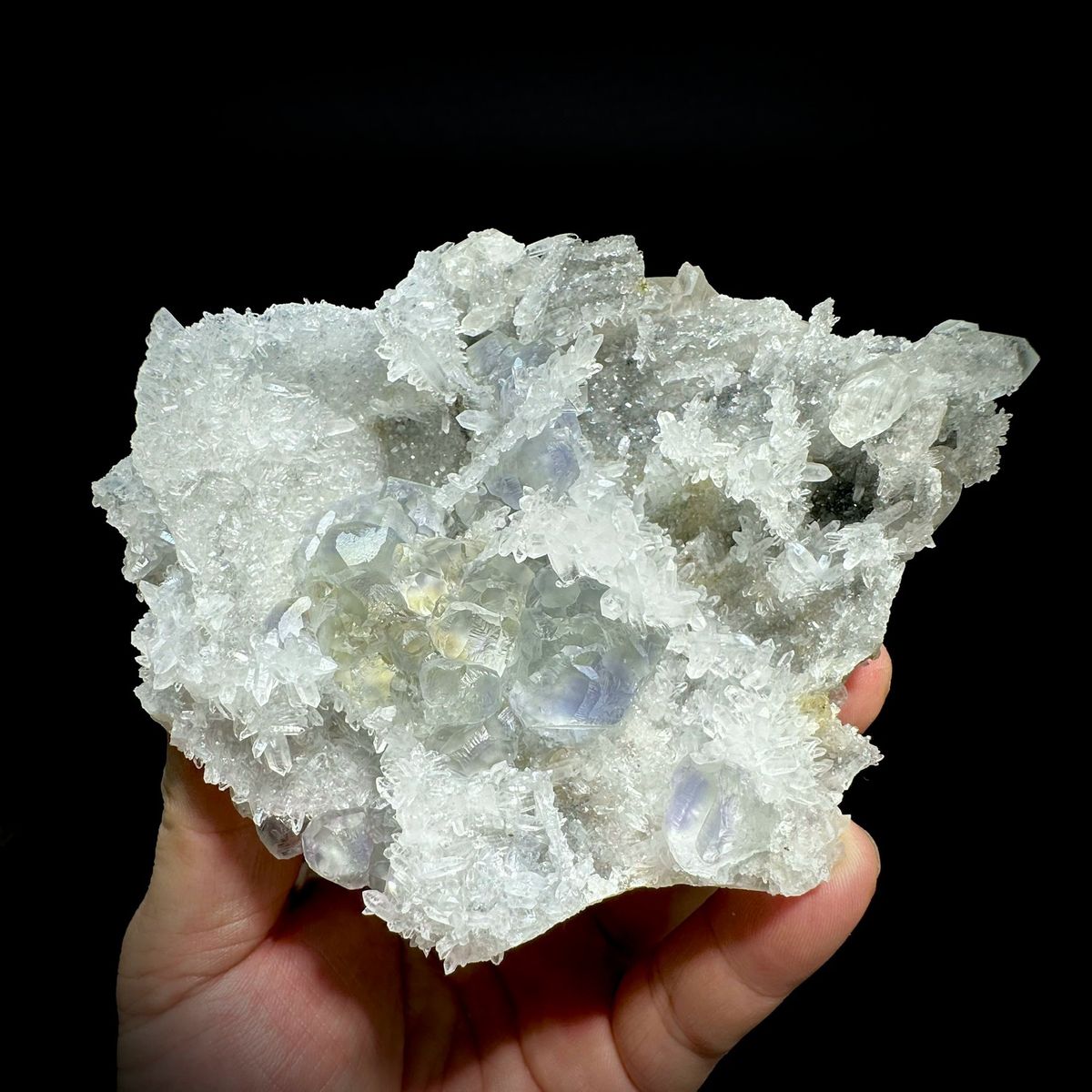 Blue-cored green fluorite among sparkling quartz and calcite from Fujian, China, held in hand