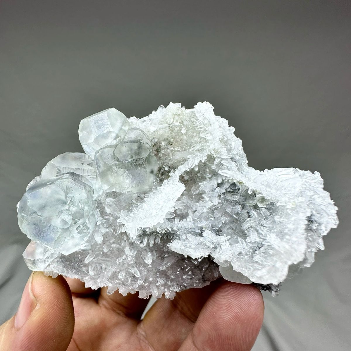 Pale blue-cored fluorite cubes on frosted white quartz from Fujian, China, held in hand