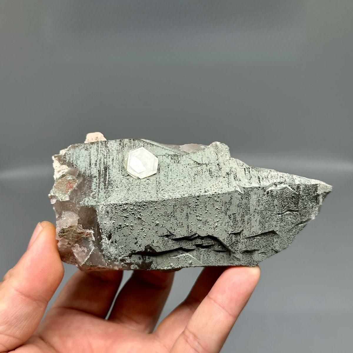 Grey hexagonal calcite plate with small white crystal and smoky quartz from Yunxiao, Fujian, China, held in hand