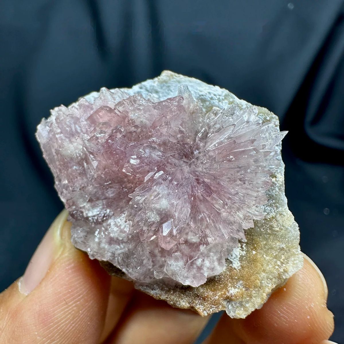 Pink radiating creedite flowers on tan matrix from Guizhou, China, held in hand