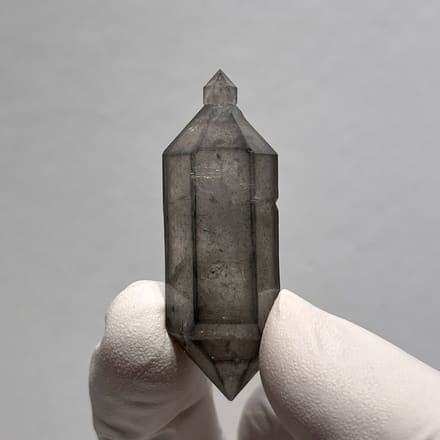 Grey sketch-pattern double-terminated quartz with sceptre tip from Yunnan, China, held in gloved hand