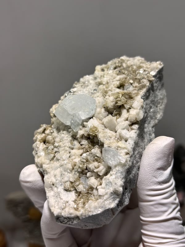 Feldspar-mica plate with pale aquamarine from Xuebaoding, Sichuan, China, held in gloved hand