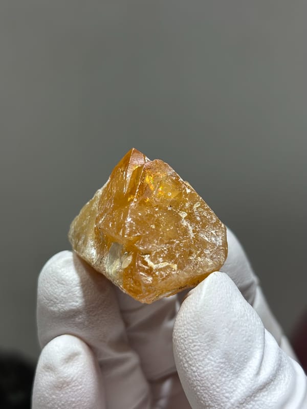 Bright orange scheelite crystal with floater base from Xuebaoding, Sichuan, China, held in gloved hand
