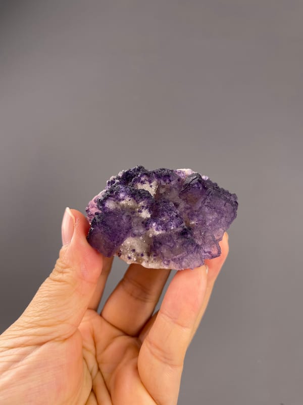 Calcite from Guizhou, China: whole purple and white association held above fingers.
