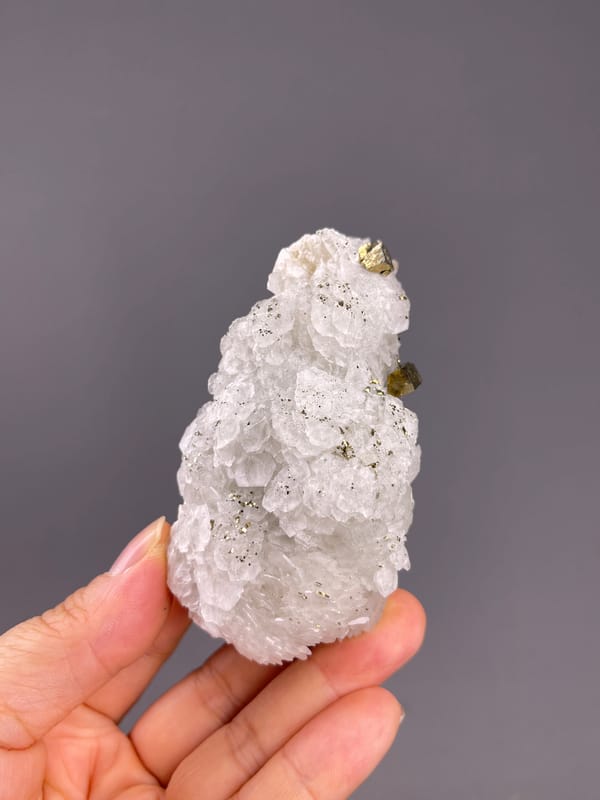 Calcite from Longyan, Fujian, China: whole elongated white specimen held across the fingers.