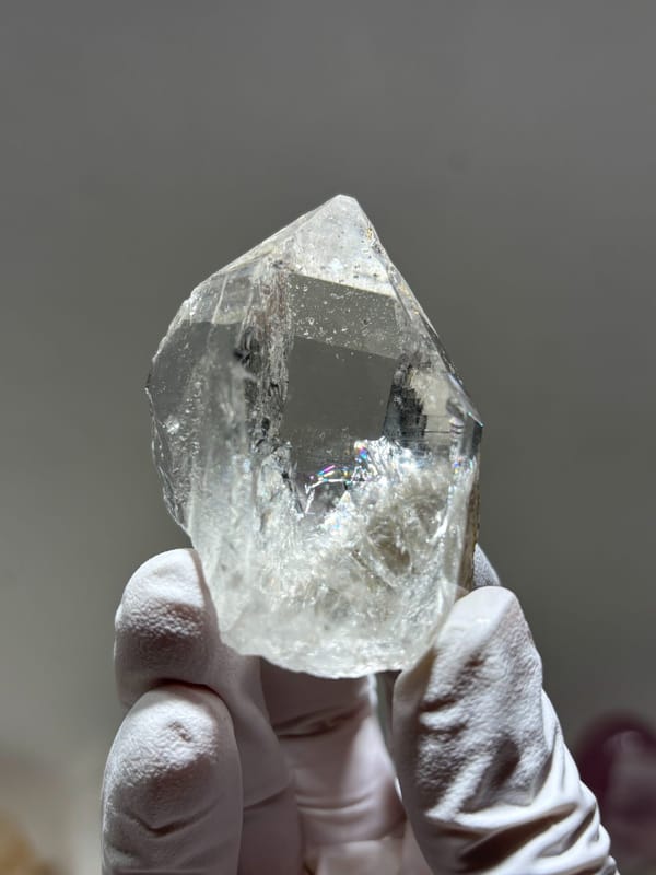 Clear quartz point with complete tip and mica from Xuebaoding, Sichuan, China, held in gloved hand