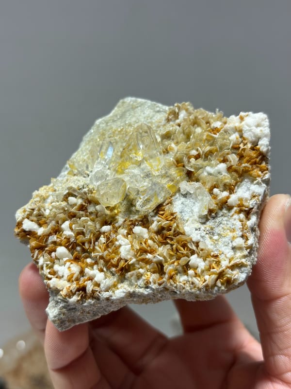 Clear quartz crystal in golden mica with white feldspar from Xuebaoding, Sichuan, China, close-up of the crystal faces