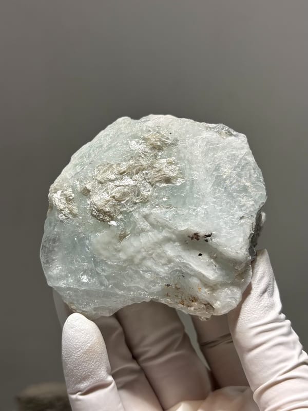 Large frosted pale aquamarine block from Xuebaoding, Sichuan, China, held in gloved hand