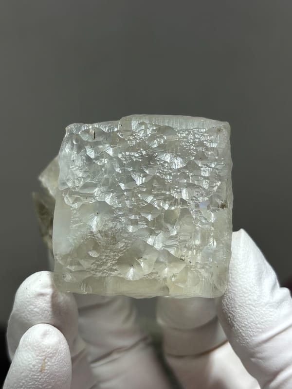 Frosted white fluorite cube from Xuebaoding, Sichuan, China, held in gloved hand