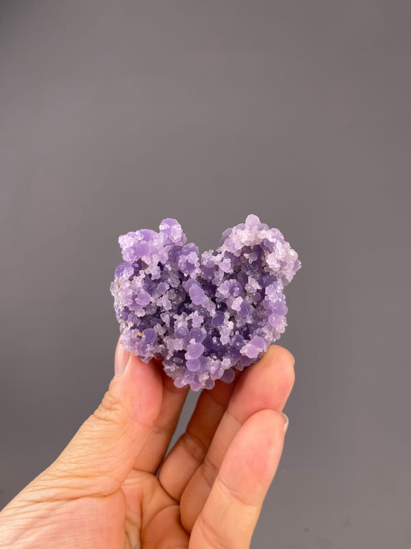 Grape Agate from Indonesia: whole purple heart-like specimen above the palm.