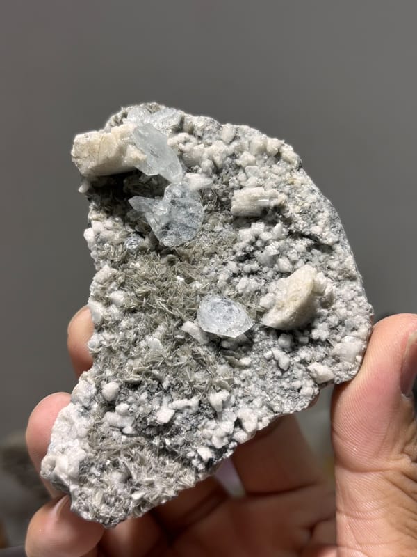 Grey matrix plate with pale aquamarine from Xuebaoding, Sichuan, China, held in hand
