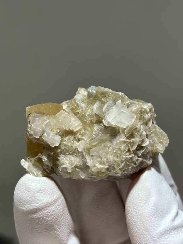 Honey scheelite with white calcite and mica from Xuebaoding, Sichuan, China, held in gloved hand