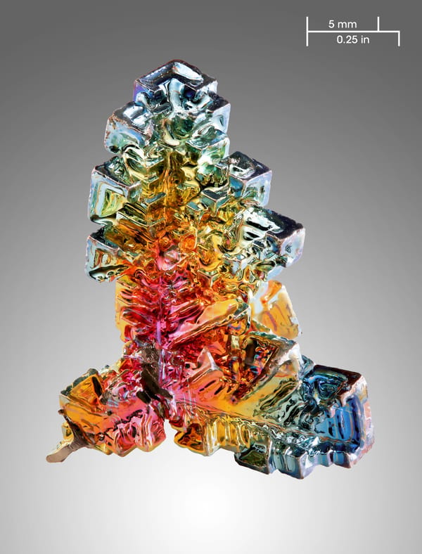 A lab-grown rainbow bismuth crystal with stair-stepped, iridescent hopper faces — a man-made product, not a natural mineral specimen.