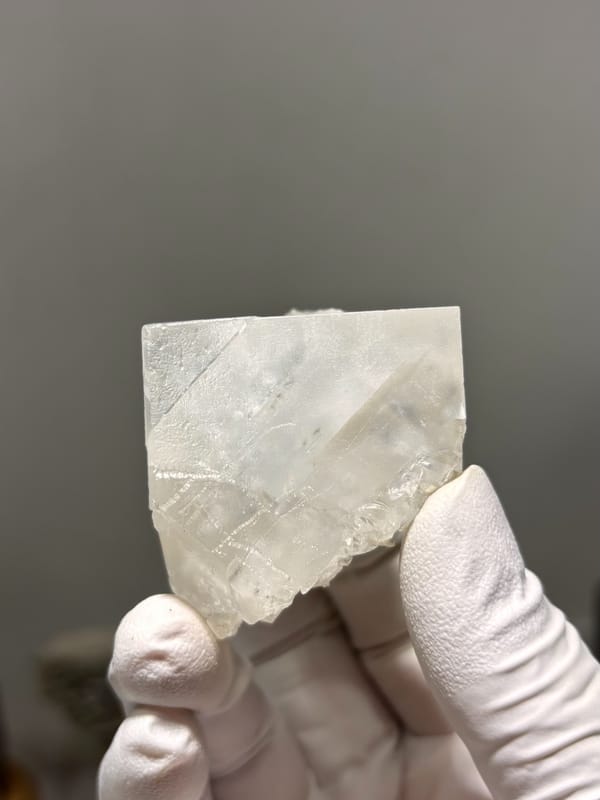 Milky white fluorite cube from Xuebaoding, Sichuan, China, held in gloved hand