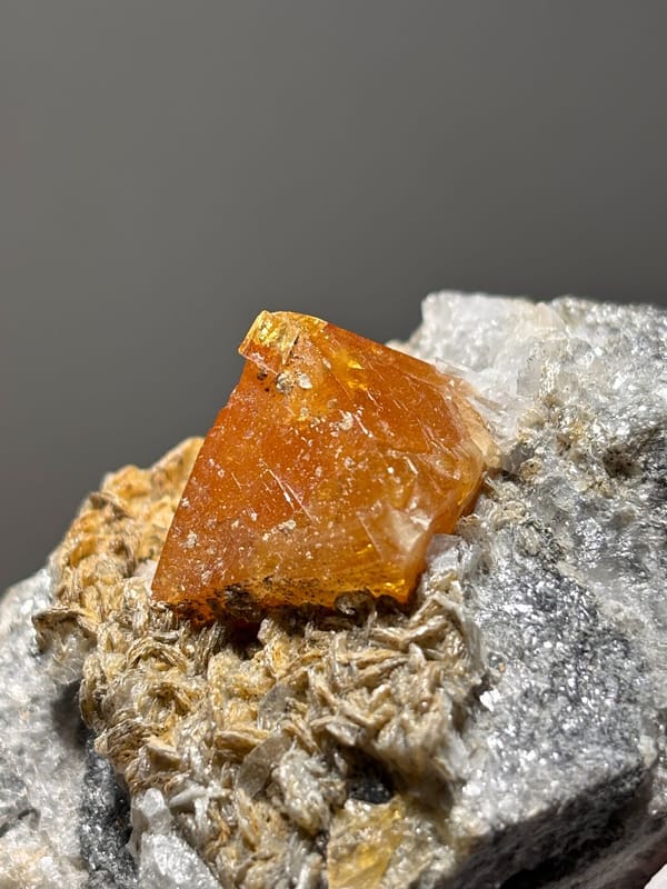 Orange scheelite on mica with fluorite at its tip from Xuebaoding, Sichuan, China, close-up of the crystal faces