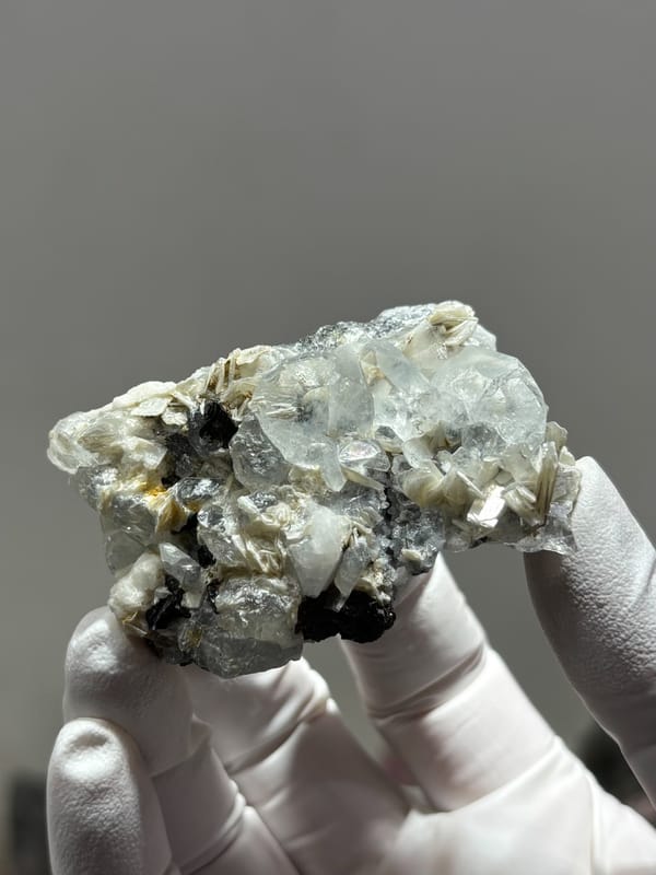 Pale aquamarine with black cassiterite and mica from Xuebaoding, Sichuan, China, held in gloved hand