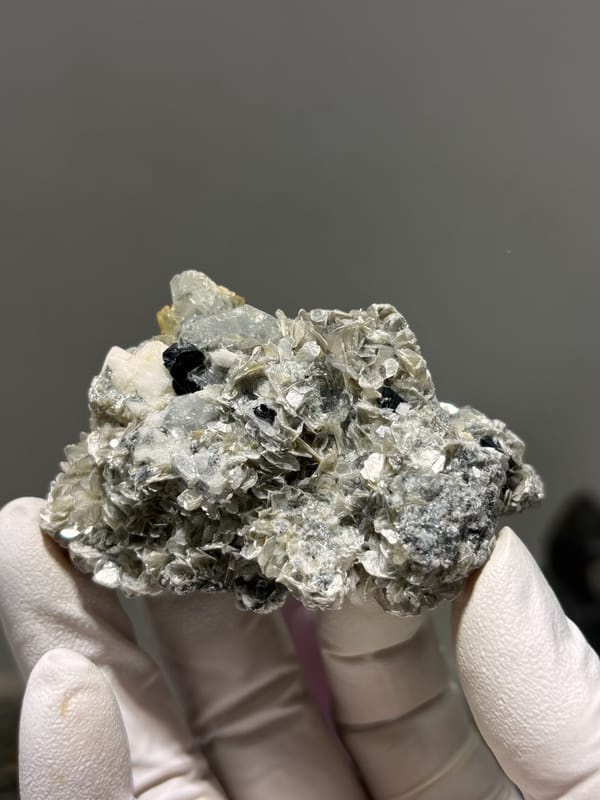 Pale aquamarine with black cassiterite, mica and feldspar from Xuebaoding, Sichuan, China, held in gloved hand