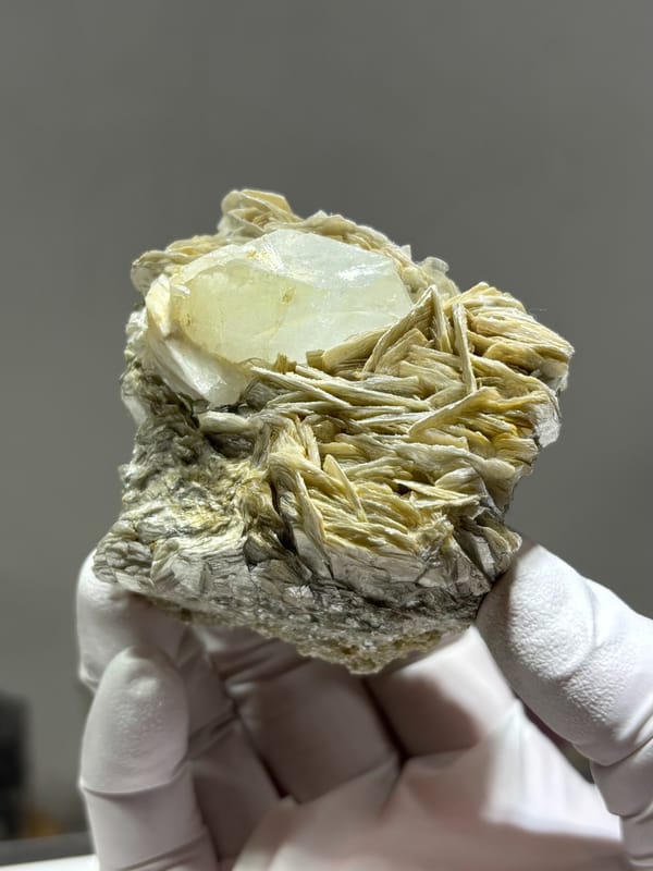 Pale aquamarine crystal nested in mica blades and feldspar from Xuebaoding, Sichuan, China, held in gloved hand