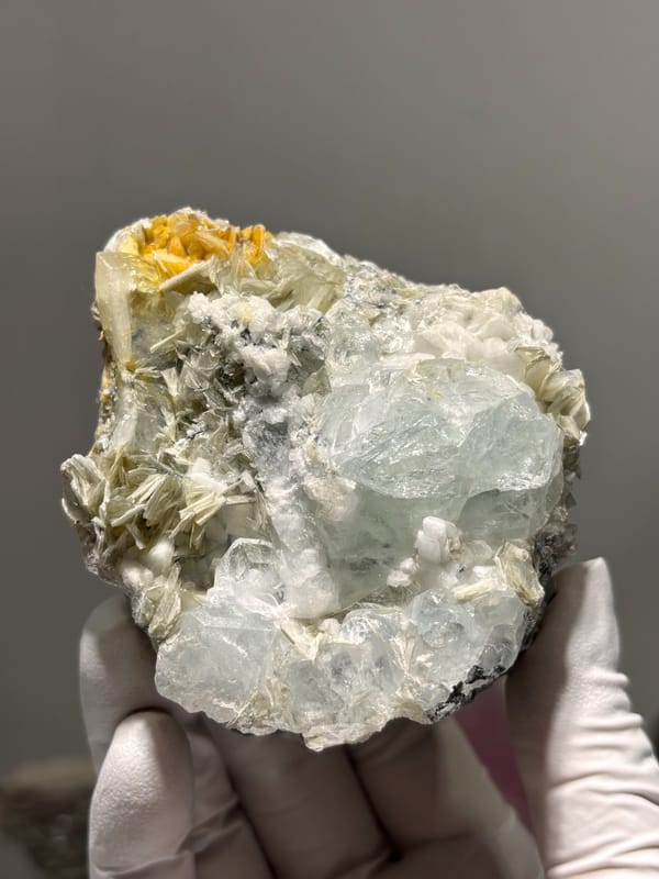 Pale aquamarine cluster with mica, feldspar and cassiterite from Xuebaoding, Sichuan, China, held in gloved hand
