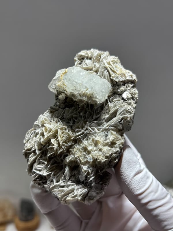 Pale aquamarine capping tall mica block from Xuebaoding, Sichuan, China, held in gloved hand