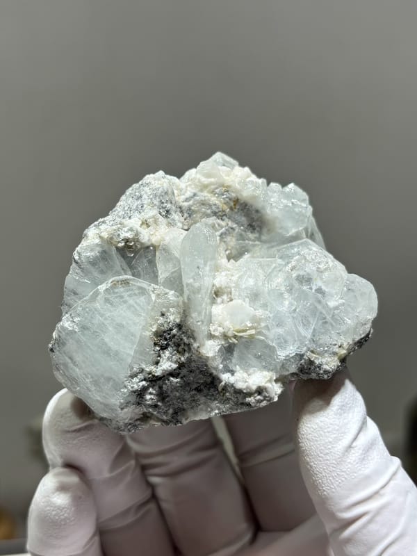 Pale blue aquamarine crystals on white feldspar from Xuebaoding, Sichuan, China, held in gloved hand