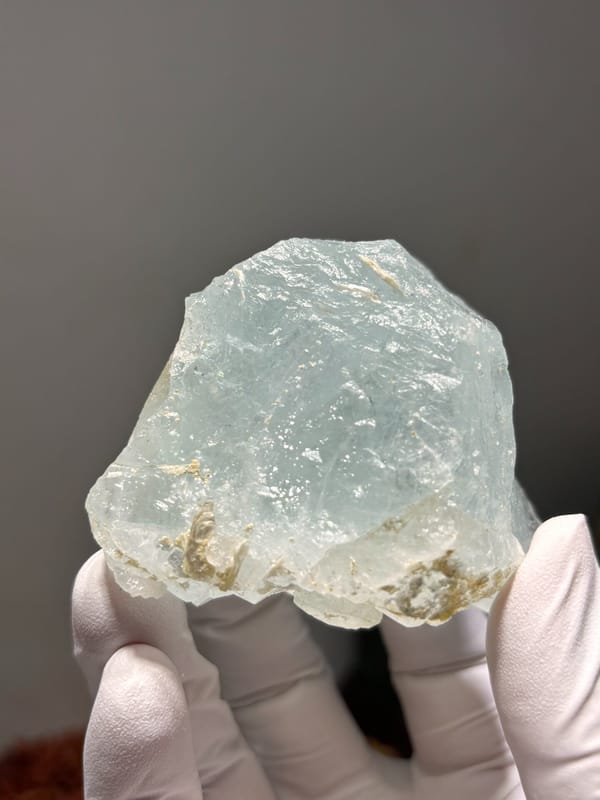 Pale blue aquamarine block from Xuebaoding, Sichuan, China, held in gloved hand