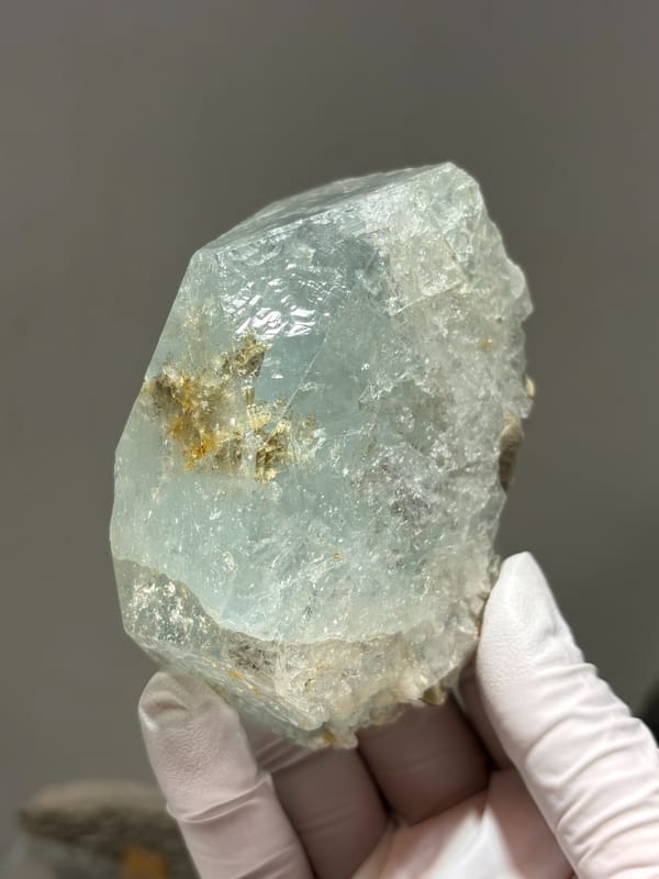 Pale blue-green aquamarine block from Xuebaoding, Sichuan, China, held in gloved hand