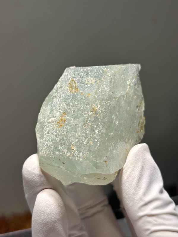 Pale green aquamarine block from Xuebaoding, Sichuan, China, held in gloved hand