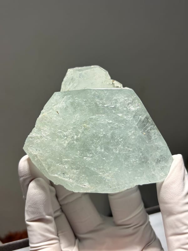 Pale green aquamarine plate from Xuebaoding, Sichuan, China, held in gloved hand