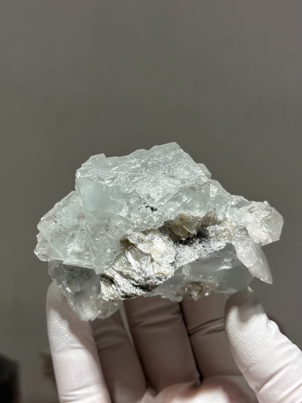 Pale green fluorite cubes with mica and albite from Xuebaoding, Sichuan, China, held in gloved hand