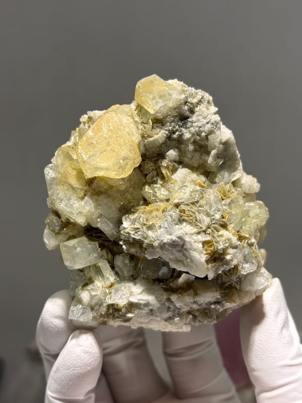 Pale yellow aquamarine crystals on mica and feldspar from Xuebaoding, Sichuan, China, held in gloved hand