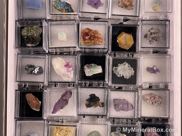 Bulk001 actual mixed mineral specimen box with about 35 different mini natural specimens in clear display boxes, including likely fluorite, quartz, aquamarine, pyrite, grape agate and other assorted minerals.