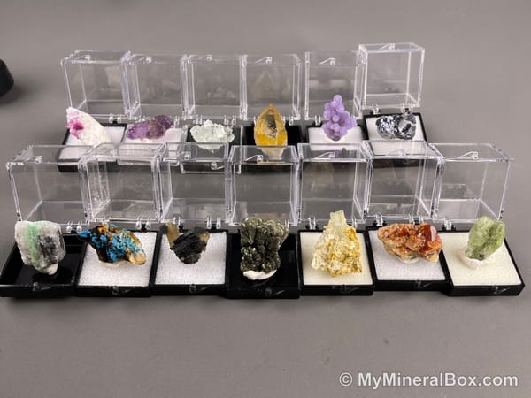 Bulk001 actual mixed mineral specimen box with about 35 different mini natural specimens in clear display boxes, including likely fluorite, quartz, aquamarine, pyrite, grape agate and other assorted minerals.