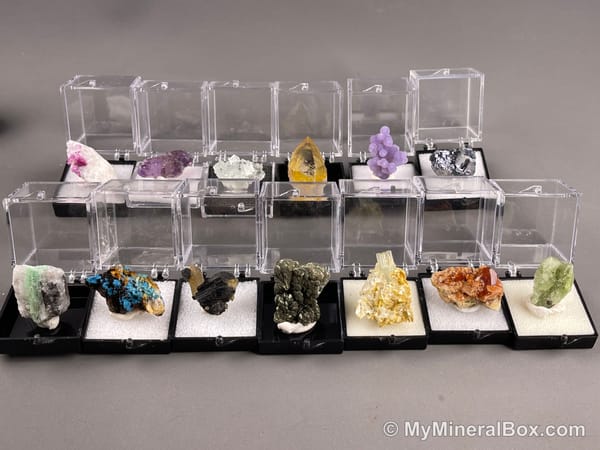 Bulk001 actual mixed mineral specimen box with about 35 different mini natural specimens in clear display boxes, including likely fluorite, quartz, aquamarine, pyrite, grape agate and other assorted minerals.