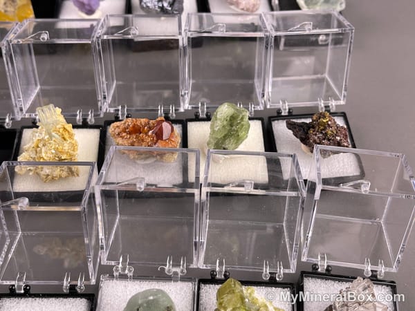 Bulk001 actual mixed mineral specimen box with about 35 different mini natural specimens in clear display boxes, including likely fluorite, quartz, aquamarine, pyrite, grape agate and other assorted minerals.