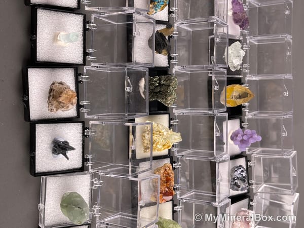 Bulk001 actual mixed mineral specimen box with about 35 different mini natural specimens in clear display boxes, including likely fluorite, quartz, aquamarine, pyrite, grape agate and other assorted minerals.