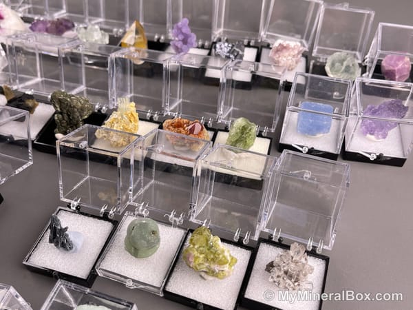 Bulk001 actual mixed mineral specimen box with about 35 different mini natural specimens in clear display boxes, including likely fluorite, quartz, aquamarine, pyrite, grape agate and other assorted minerals.