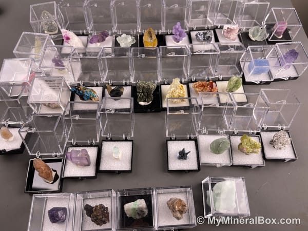 Bulk001 actual mixed mineral specimen box with about 35 different mini natural specimens in clear display boxes, including likely fluorite, quartz, aquamarine, pyrite, grape agate and other assorted minerals.