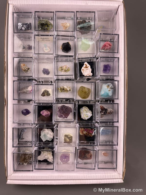 Bulk002 actual mixed mineral specimen box with approximately 35 to 40 different mini specimens in clear display boxes, including likely fluorite, quartz, aquamarine, galena, pyrite, grape agate, stibnite and other assorted minerals.