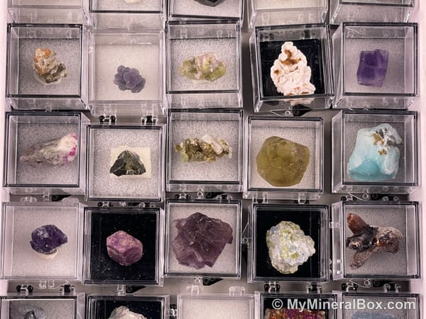 Bulk002 actual mixed mineral specimen box with approximately 35 to 40 different mini specimens in clear display boxes, including likely fluorite, quartz, aquamarine, galena, pyrite, grape agate, stibnite and other assorted minerals.