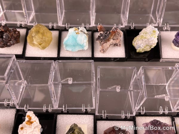 Bulk002 actual mixed mineral specimen box with approximately 35 to 40 different mini specimens in clear display boxes, including likely fluorite, quartz, aquamarine, galena, pyrite, grape agate, stibnite and other assorted minerals.