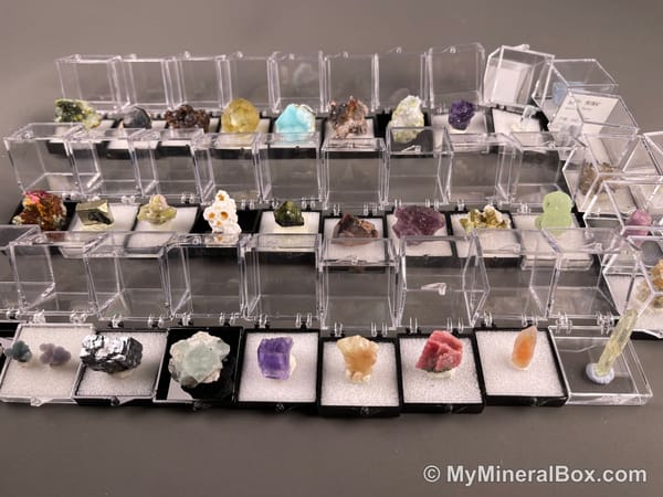 Bulk002 actual mixed mineral specimen box with approximately 35 to 40 different mini specimens in clear display boxes, including likely fluorite, quartz, aquamarine, galena, pyrite, grape agate, stibnite and other assorted minerals.