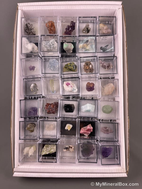 Bulk004 actual mixed mineral specimen box with about 35 different mini natural specimens, including likely fluorite, black tourmaline, quartz, stibnite, grape agate and green prehnite-type material.