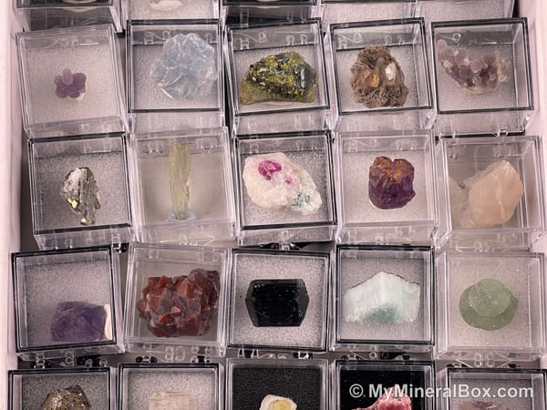 Bulk004 actual mixed mineral specimen box with about 35 different mini natural specimens, including likely fluorite, black tourmaline, quartz, stibnite, grape agate and green prehnite-type material.