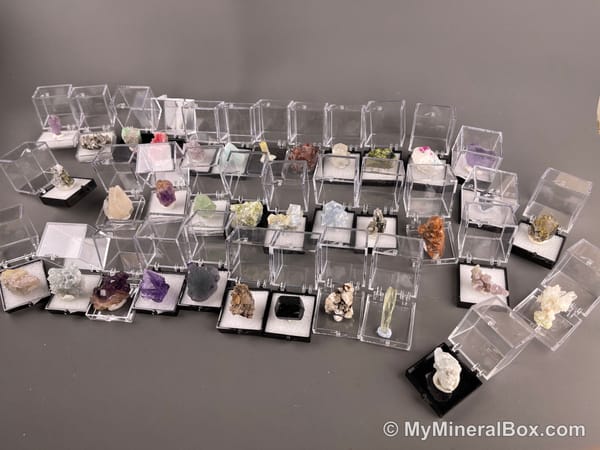 Bulk004 actual mixed mineral specimen box with about 35 different mini natural specimens, including likely fluorite, black tourmaline, quartz, stibnite, grape agate and green prehnite-type material.